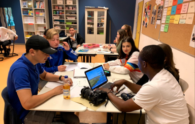 Foto: Schülerinnen und Schüler mit Laptop an zwei Tischen